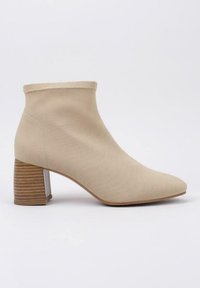 Botín beige hasta el tobillo hecho de tela texturizada, con punta afilada y un tacón de bloque de madera con rayas horizontales.