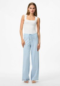 Vit ärmlös topp i kombination med ljusblå randiga vida byxor med dragsko i midjan, tillverkade av mjukt tyg.