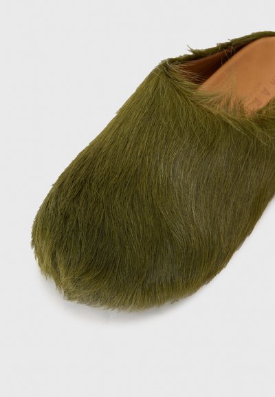 Grön päls slip-on sko med rund tå, som har en mjuk, texturerad yta och en ren inredningsdesign. Ingen synlig hårdvara eller detaljer.