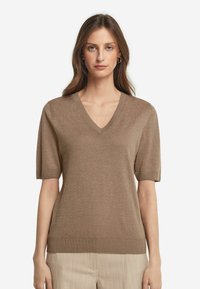 Lys brun kortærmet sweater med V-hals, ribbet kant og glat tekstur. Enkel design uden mønstre eller pynt.