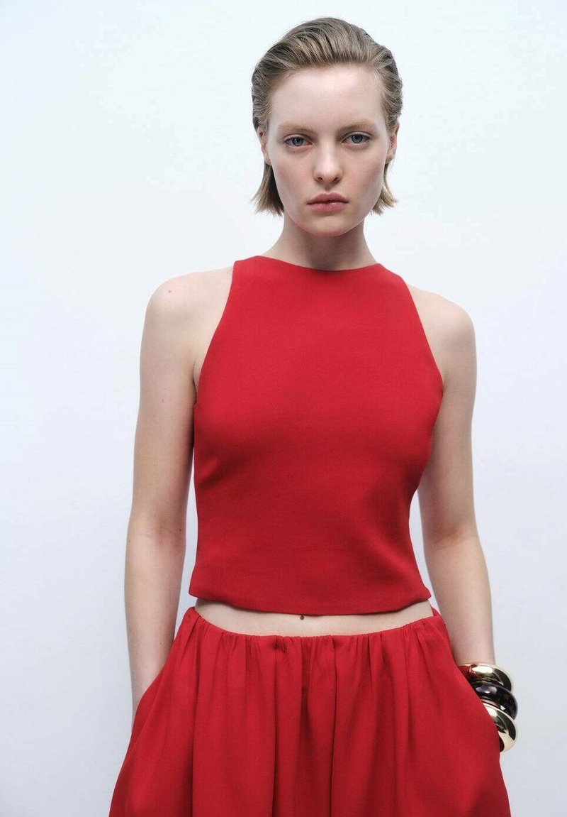 Top crop rosso senza maniche realizzato in un tessuto liscio, abbinato a una gonna lunga coordinata, che mette in evidenza un punto vita sagomato e una leggera arricciatura all'orlo.