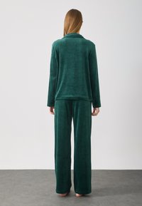 Grønn, myk stoff hjemmeantrekk med lange ermer, vide bukser og avslappet passform. Jevn tekstur med minimale sømmer.