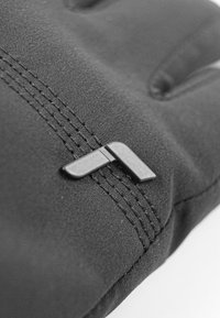Guante de tela negra con costuras cosidas y un distintivo detalle en negro que recuerda a una forma angular. Textura suave y diseño ergonómico.