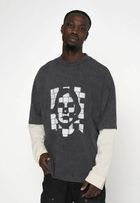 Szara, przeszła t-shirt w dużym rozmiarze, wykonany z bawełny, z efektownym wykończeniem, z dużą białą grafiką twarzy w wzór cegieł na przodzie.