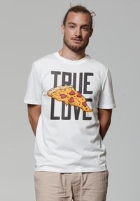 Weißes Baumwoll-T-Shirt mit einem großen, illustrierten Pizzastück, das Herzen zeigt, sowie dem Text "ECHTE LIEBE" in fetten schwarzen Buchstaben.