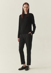 Pull en laine noire à encolure large, associé à un pantalon noir sur mesure et des mocassins noirs, créant un look monochrome élégant.