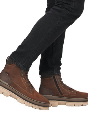 Las botas de tobillo de ante marrón presentan un cierre de cordones en la parte delantera, cremallera lateral y una gruesa suela de goma beige con un acabado texturizado y acentos oscuros en contraste.