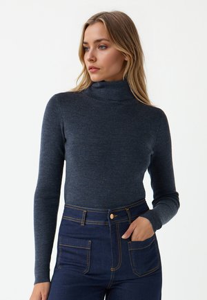 Dunkelblauer gerippter Rollkragenpullover mit langen Ärmeln, kombiniert mit hochtaillierten dunklen Jeans aus Denim mit kontrastierenden gelben Nähten.
