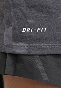 Gros plan sur un short de sport gris foncé avec le logo blanc "DRI-FIT" imprimé près de l'ourlet sur le côté gauche.