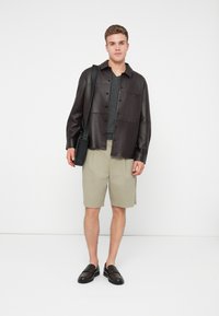 Sötétbarna bőrkabát, szürke pulóver, bézs sort, fekete loaferek, fekete messenger táska; minimalista és strukturált dizájn.