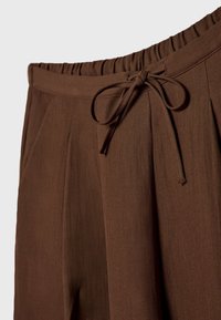 Pantalon marron avec une taille élastique et un cordon en tissu noué à l'avant.