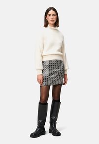 Cremiger gestrickter Pullover, gemusterter schwarz-weißer Minirock, schwarze blickdichte Strumpfhosen, knielange glänzende schwarze Stiefel. Schlichte, moderne Silhouette.