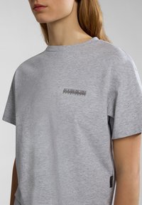 Grijze katoenen t-shirt met korte mouwen, voorzien van een rechthoekig logo-opdruk op de borst. Glad materiaal met een ontspannen pasvorm. Zijsplitdetail.
