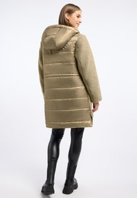 Padded oliwkowa kurtka z kapturem, z pluszowym futrzanym wykończeniem na rękawach i bokach, o prostym kroju z bocznymi rozcięciami.