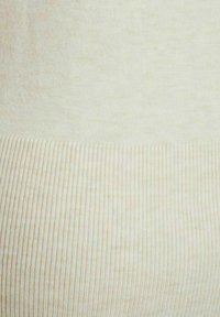 Tejido de punto acanalado en color crema con una textura suave, que presenta un brillo sutil. El material muestra un suave degradado de tonos claros a más claros.