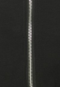 Tissu noir avec une fermeture éclair métallique argentée courant verticalement, présentant un bord texturé et des dents uniformément espacées.