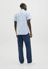 Kurze Hemden mit einem blau-weißen Blumenmuster, aus leichtem Stoff; kombiniert mit locker sitzenden dunkelblauen Hosen und weißen Sneakers.