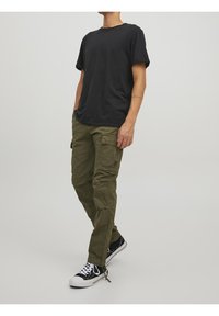 Czarny bawełniany T-shirt w połączeniu z oliwkowozielonymi spodniami cargo z kieszeniami bocznymi, fakturowaną tkaniną oraz czarnymi trampkami z białymi podeszwami.