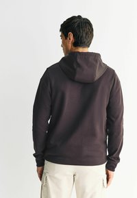 Tumepruuni värvi kapuutsiga dressipluus, pikkade varrukatega ja vormikohase disainiga. Omab kapuutsi ja sileda tekstuuri. Kombineeritud heledate värvi cargo-pükstega.