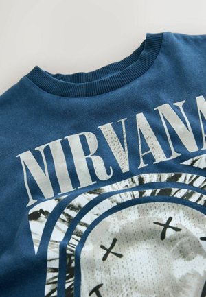 Zils kokvilnas džemperis ar ribotu apkakli. Iezīmēts ar grafisku dizainu, kurā ir vārds "NIRVANA" un apļveida seja ar X acīm.