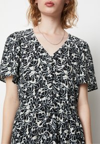 Svartvit blommönstrad klänning med korta ärmar, V-ringning, knappar framtill och en rynkad midja. Slätt, lätt tyg.