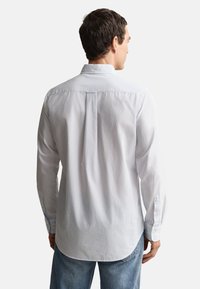 Chemise blanche à manches longues avec un pli dans le dos et un col pointu, dotée de poignets à boutons. Confectionnée dans un tissu léger, conçue pour une coupe décontractée.