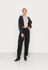 Jaqueta de ganga cropped preta com botões, blusa justa cinza claro, calças largas pretas e botas de tornozelo com salto pretas. Estilo simples com acessórios mínimos.