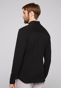 Zwarte longsleeve shirt met een gladde textuur, klassieke kraag en knoopsluiting bij de mouwen, met een iets gebogen hem en een design met rugpas.