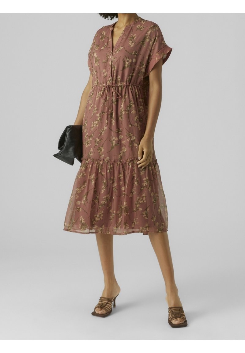 Robe midi florale en rose poussiéreux, tissu léger, manches courtes, taille cintrée, ourlet en volants, associée à une pochette noire et des sandales à lanières.