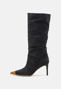 Black satin high-heeled boot with slouchy upper, pointed toe, and contrasting tan leather tip. Features a slender stiletto heel.