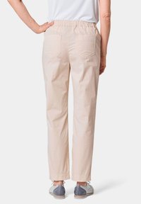 Lichtbeige elastische taillebroek met achterzakken en rechte pijpen. Gecombineerd met grijs-witte schoenen. Eenvoudig, casual ontwerp.