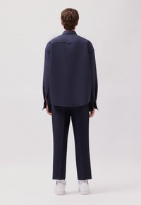 Camicia oversize blu navy e pantaloni abbinati in tessuto morbido, con orlo curvo e maniche lunghe, abbinati a sneaker bianche.