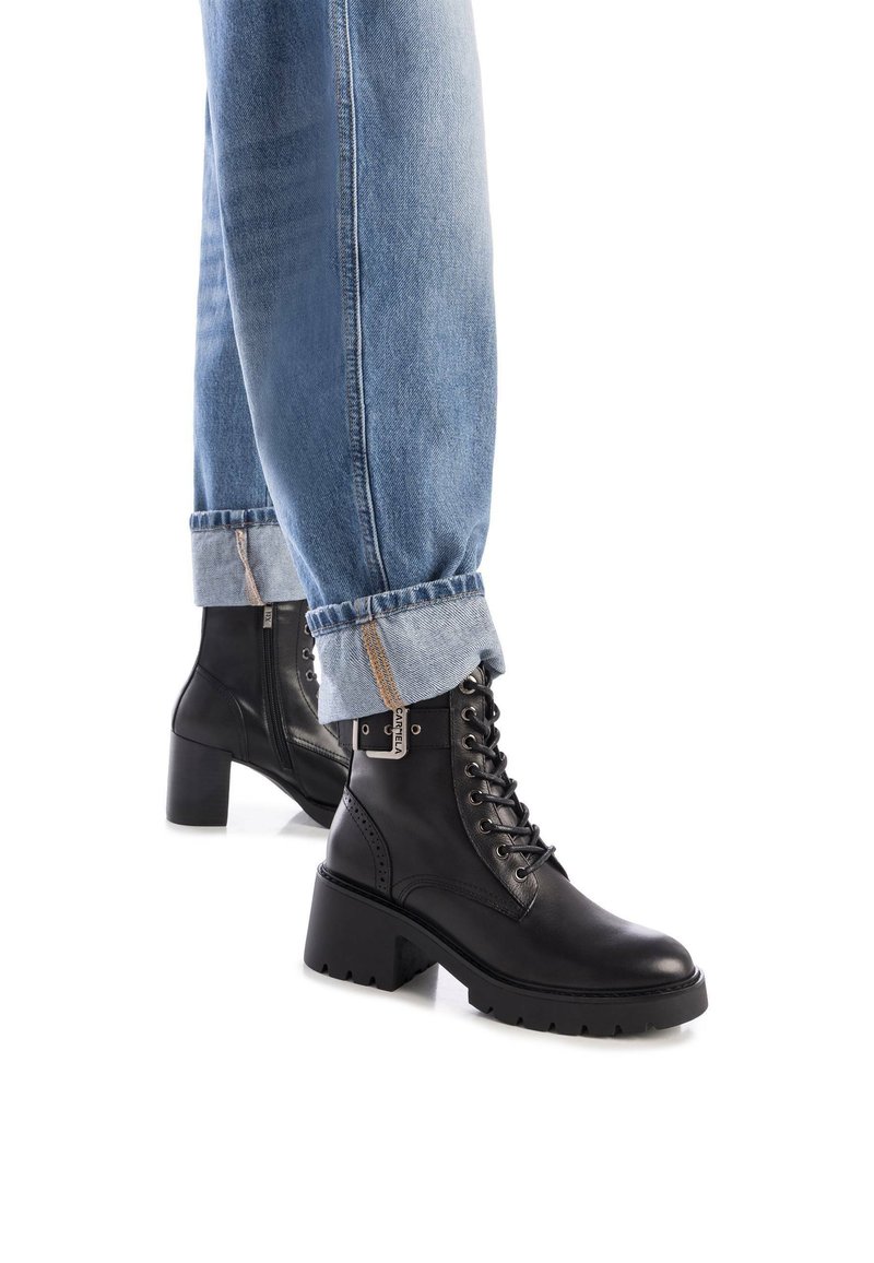 Botas de cuero negras hasta el tobillo con un tacón grueso y un diseño de cordones. Acabado texturizado con costuras prominentes y un detalle de cremallera lateral.