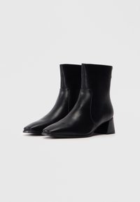 Botas de tobillo de cuero negro con punta afilada y un tacón bajo en bloque. Textura suave, costuras mínimas y sin hardware visible.