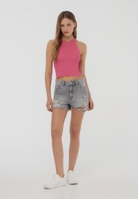 Top corto a coste rosa, con collo alto. Indossato con pantaloni corti in denim strappati, orlo sfrangiato. Completato da sneakers bianche.