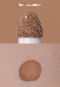 Producto cremoso marrón con una punta aplicadora suave y texturizada en la parte superior; muestra del mismo color en piel suave debajo.