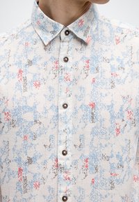 Ανοιχτόχρωμο πουκάμισο με κουμπιά, με υφή υφάσματος που διαθέτει μοτίβο σε μπλε, κόκκινες και μαύρες αποχρώσεις. Στρογγυλεμένος γιακάς και καφέ κουμπιά.