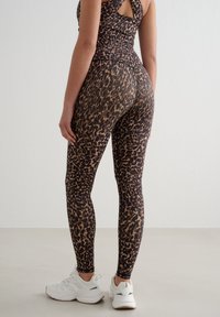 Leggings med leopardmønster laget av elastisk stoff, med høyt liv og tettsittende design, kombinert med hvite joggesko.