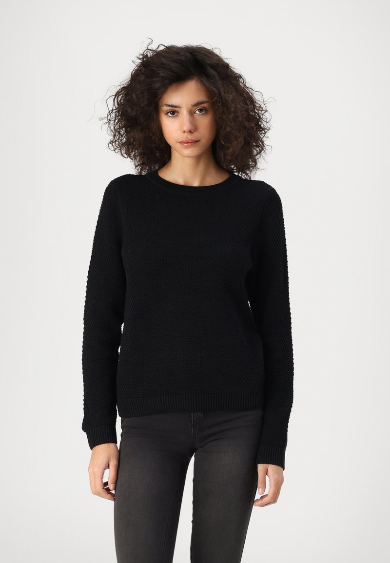Svart strikket genser med strukturert mønster, rund hals og ribbestrikkede ermer og hem. Brukt sammen med mørke jeans. En enkel, allsidig design.