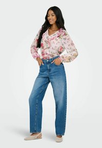 Blusa floral con volantes en tonos de rosa y verde, combinada con jeans de cintura alta azules y zapatos planos de mimbre beige.