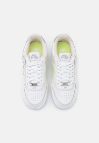Baskets Nike Air Force 1 avec une tige en cuir blanc, des accents argentés et une semelle intérieure vert vif. Présente un design classique de bout perforé.