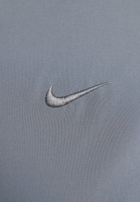 Grijze stof met een zachte textuur, met een opvallende, zilveren geborduurde Nike swoosh-logo.
