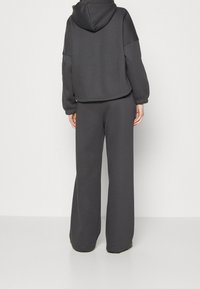 Szara krótka bluza z kapturem i szerokie spodnie dresowe. Tkanina ma gładką fakturę. Posiada elastyczne mankiety i minimalistyczny design.