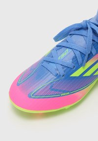 Blå och rosa fotbollsskor med en strukturerad ovandel, neongröna accenter och en slank aerodynamisk design med gradientränder.