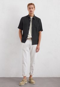 Svart kortermet skjorte med knapper, hvit t-skjorte med rund hals, rullede hvite bukser, og lyse beige sko med teksturert såle.