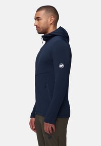 Navyblaue Kapuzenjacke aus weichem, flexiblem Stoff. Verfügt über einen Frontreißverschluss, Seitentaschen und einen Logopatch am Ärmel.