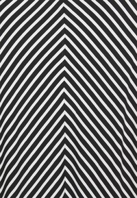 Czarny i biały materiał z diagonalnymi paskami, tworzącymi wzór w chevron. Paski różnią się szerokością, co nadaje wyraźną teksturę wizualną.