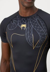 Sort atletisk shirt lavet af glat materiale med et slange-design i grå og gule accenter, med korte ærmer og en tætsiddende pasform.