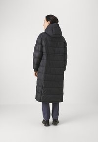 Lungo cappotto imbottito nero con cappuccio, design a righe verticali, polsini elasticizzati e chiusure a scatto lungo i lati. Materiale morbido e leggero.