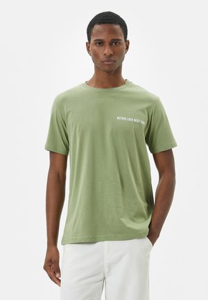 Lichtgroene T-shirt met korte mouwen van katoen, met een ronde hals en witte tekst "BETTER LUCK NEXT TIME" op de borst.